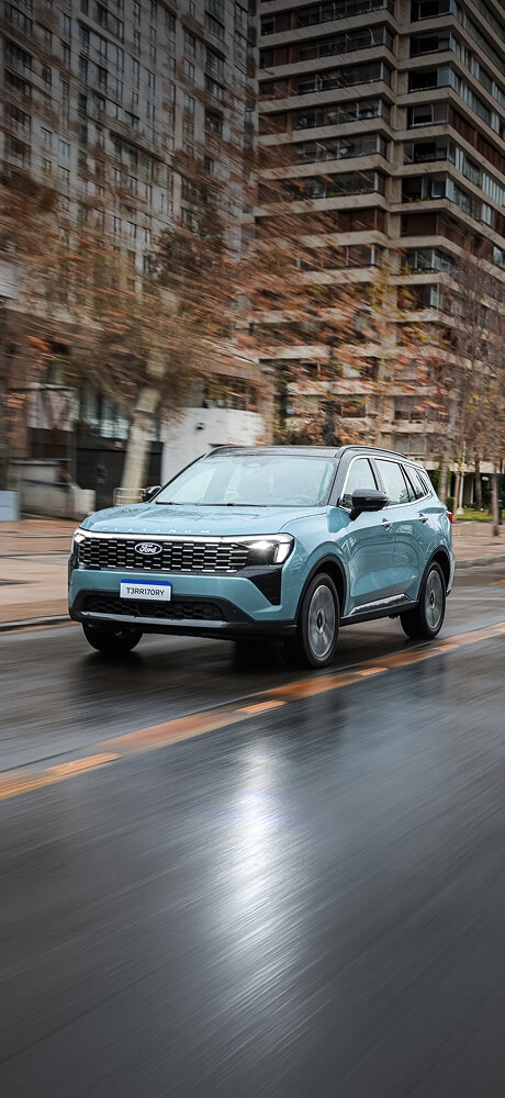 Ford Territory Platinum celeste en movimiento sobre una vía urbana mojada. Mostrar más líneas