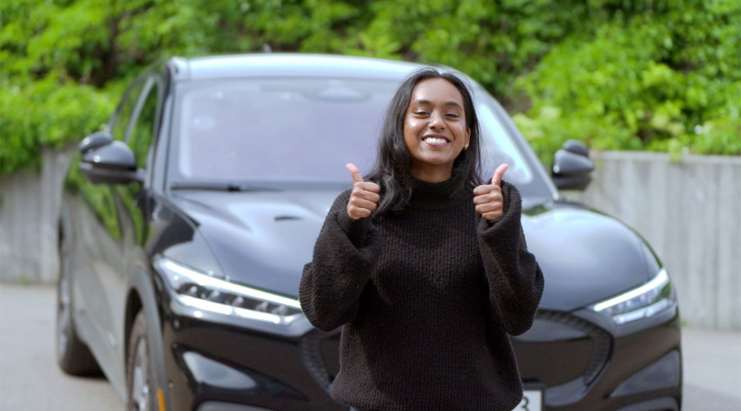 Una mujer levanta ambos pulgares con su Mustang Mach-E como fondo