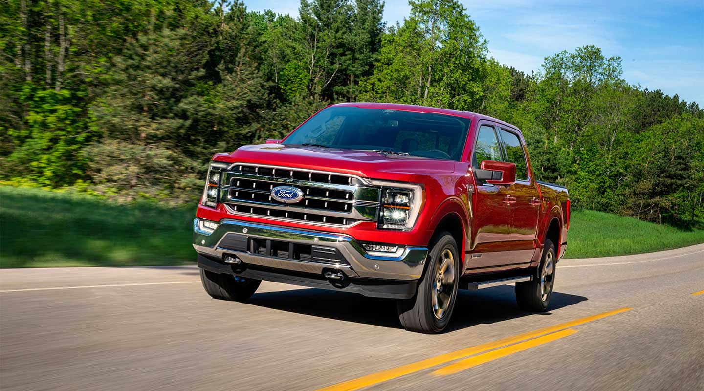 Ford F-150 Híbrida en color rojo circulando por una carretera y con un bosque como fondo